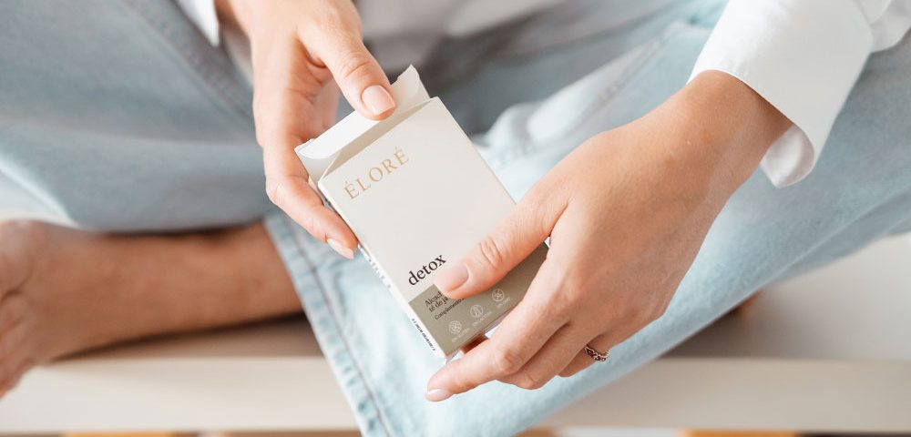Mulher a segurar a embalagem de Éloré Detox, suplemento de nutricosmética com alcachofra e chá de java
